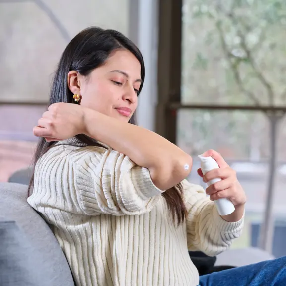 User applying a dermal formulation using a spray pump onto the elbow, illustrating delivery of liquid or semi-solid formulations to the skin.