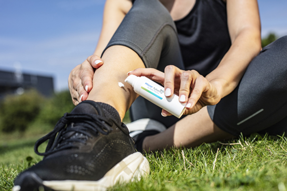 Woman seated on green grass dispensing white cream from Aptar Pharma Micro+ Futurity device on leg.