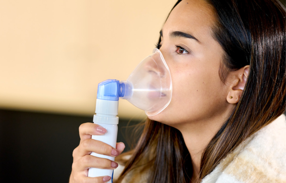 Woman with brown hair holds clear mask of PureHale fine mist dispenser to face for upper airways deposition.