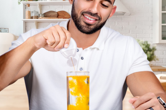 Man squeezing orange dirnk enhancer into glass of water
