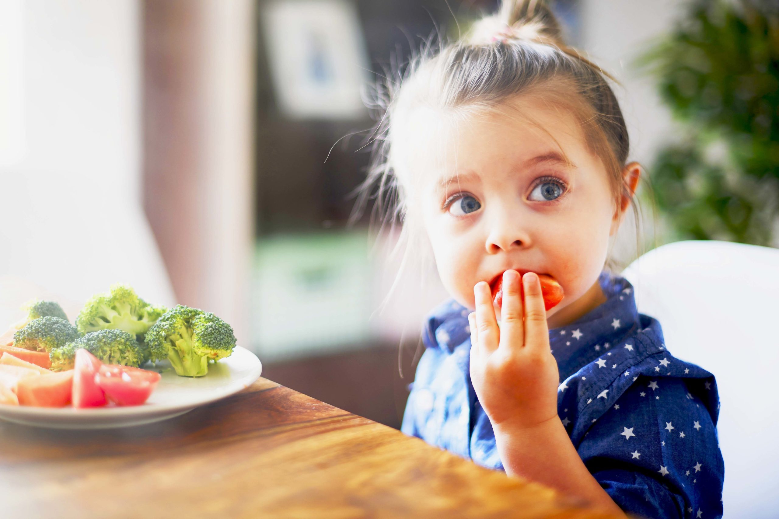 Young girl eating vegetables at kitchen table