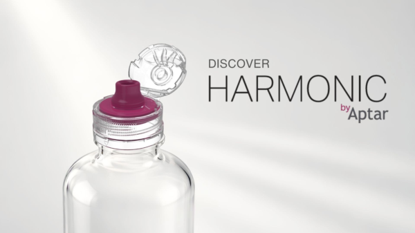 Transparent flip-top beverage closure with a dispensing spout shown open on a clear bottle, alongside the text “Discover HARMONIC by Aptar” on a light gray background.