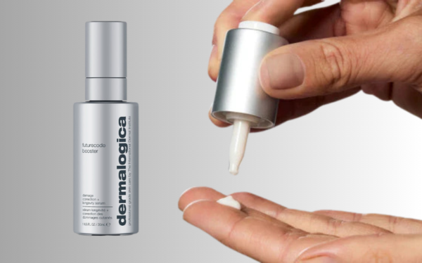 A Closed Dropper Packaging with Grey Matte Finish labeled FutureCode Booster by Dermalogica Next to a Hand Holding the Cap and Pipette and Dispensing a Drop of White Serum Formula on a Grey Background