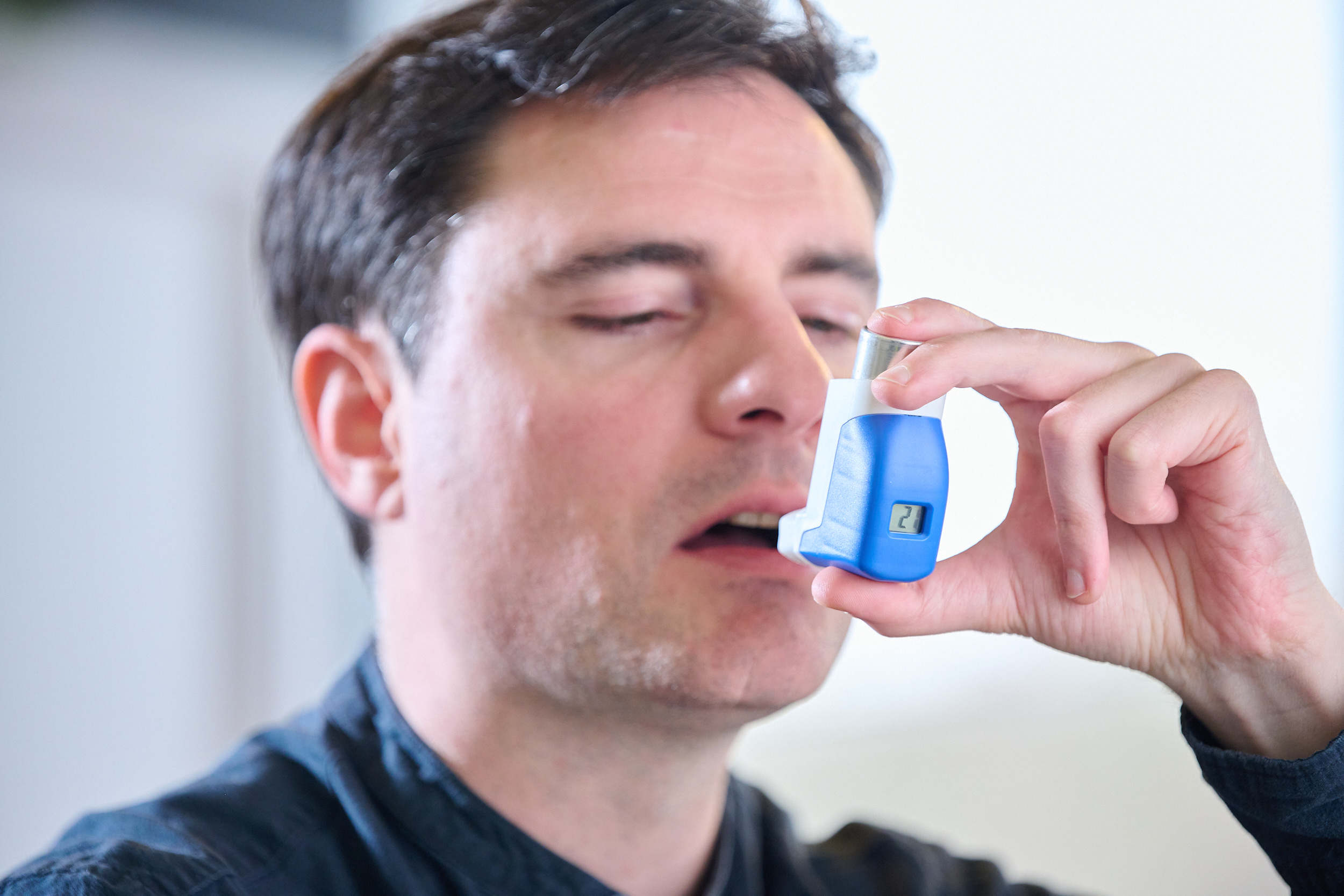 Close of man's face holding blue Aptar Pharma MDI with integrated blue digital dose counter screen visible.